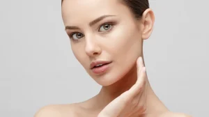 Woman with smooth skin gently touching her cheek and gazing forward with serene expression, showcasing results of exosome therapy, against light gray background
